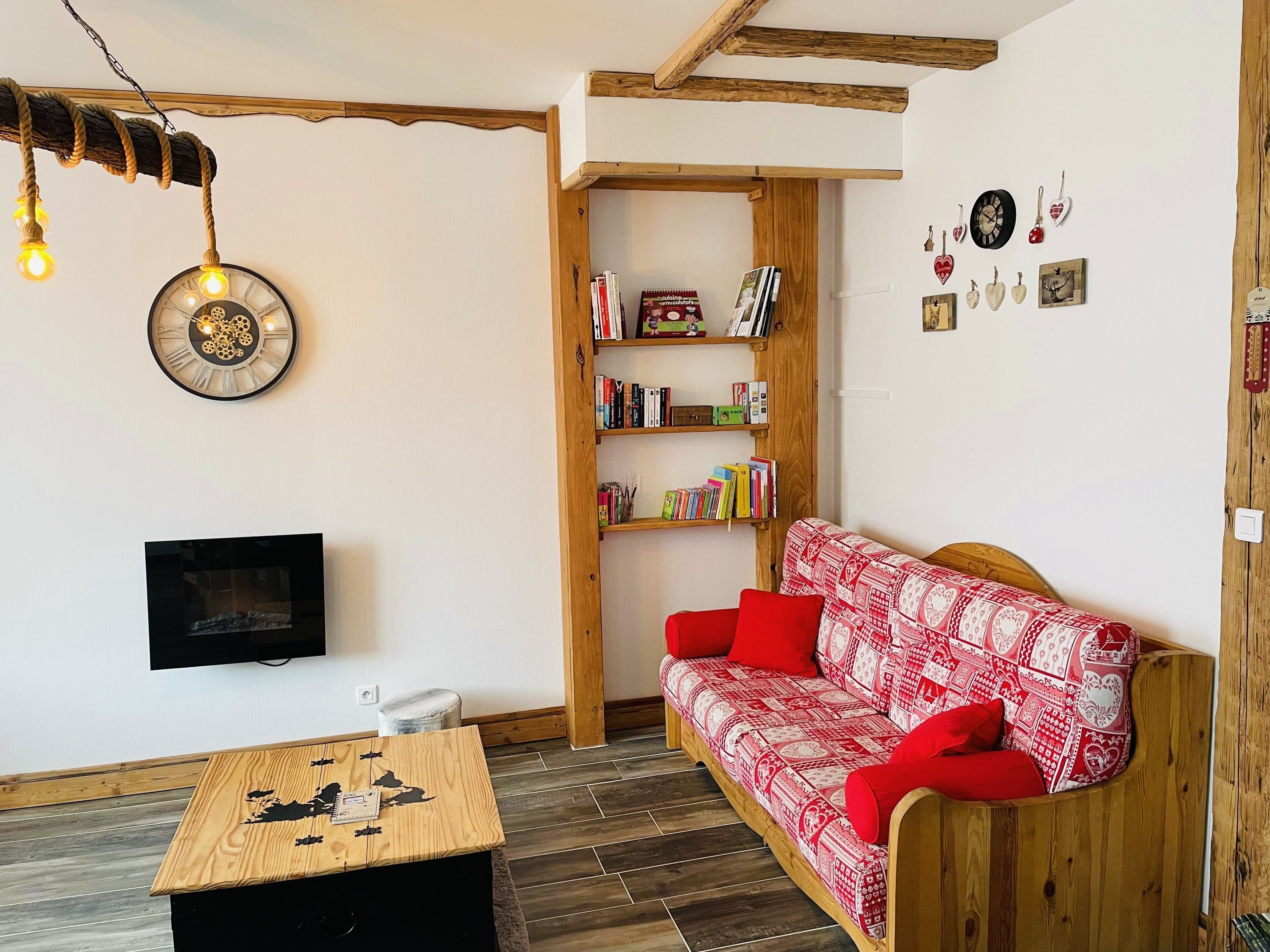A cozy living room with a wooden sofa, a television, a bookshelf, and a decorative clock.
