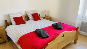 Ein ordentlich bezogenes Bett mit einer rot-weißen Bettdecke, zwei roten Kissen und zwei zusammengerollten Handtüchern.