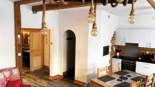 Ein gemütliches Zimmer mit Holzbalkendecke, einem Esstisch und einem roten Sofa.