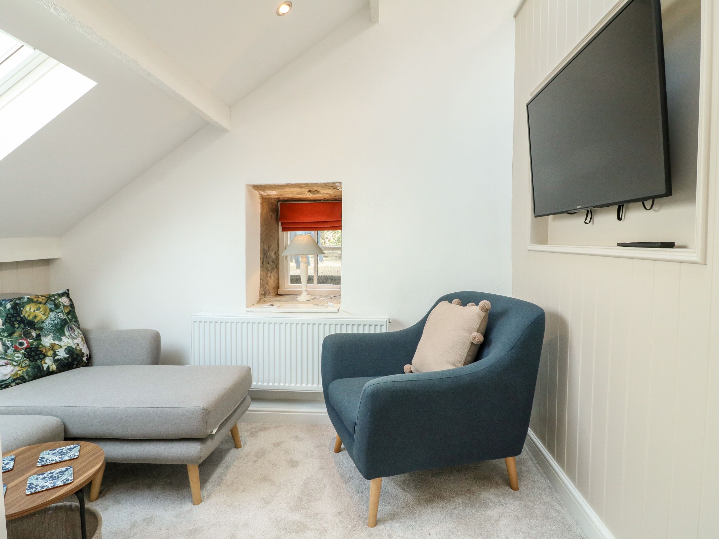A cozy room with a grey sofa, a blue armchair, a small wooden table, and a TV mounted on the wall.