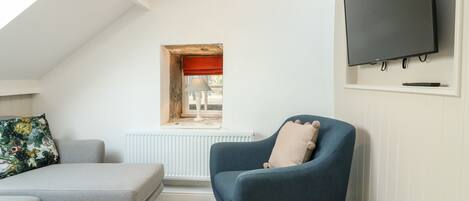A cozy room with a grey sofa, a blue armchair, a small wooden table, and a TV mounted on the wall.