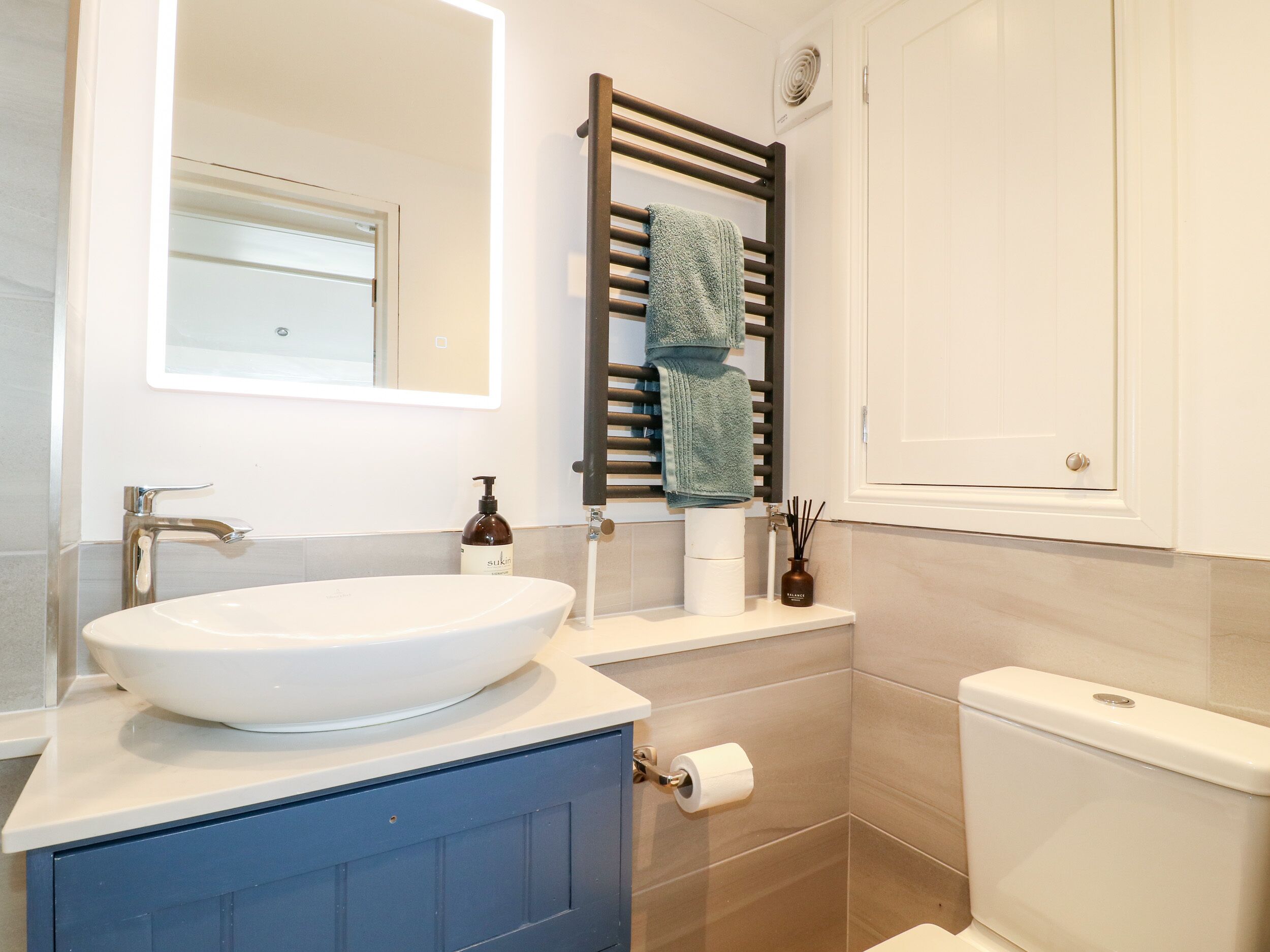 A bathroom with a white sink, a mirror, a towel rack, a toilet, and a roll of toilet paper.