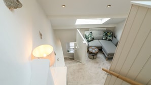 A staircase leading to a room with a skylight, a sofa with floral cushions, a small round table, and a lamp. - The Hayloft (Matlock)