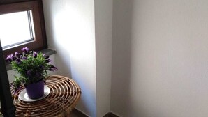 A corner room with a window, a wicker chair with a potted plant, a woven basket, and a bookshelf with books. - Cozy apartment in the center 2km from the sea (Bosa)