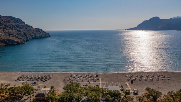 A beach with rows of umbrellas and sun loungers, a clear sky, and a calm sea. - Paligremnos Residence I, sublime beachside retreat (Plakias)