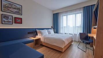 A modern hotel room with a bed, a desk, a chair, and a sofa.
