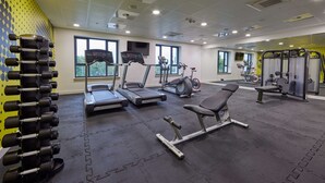 Un gimnasio con cintas de correr, elípticas, bancos de pesas y una estantería de mancuernas.