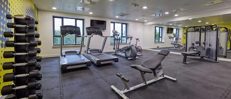 Et fitnesscenter med løbebånd, crosstrainere, vægtbænke og en stativ med håndvægte.