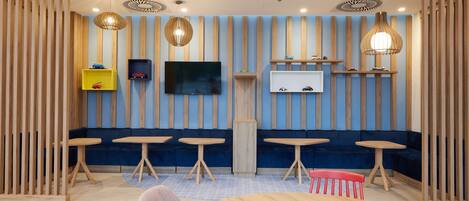 A modern interior with wooden slats, a TV, shelves with toys, and round tables.