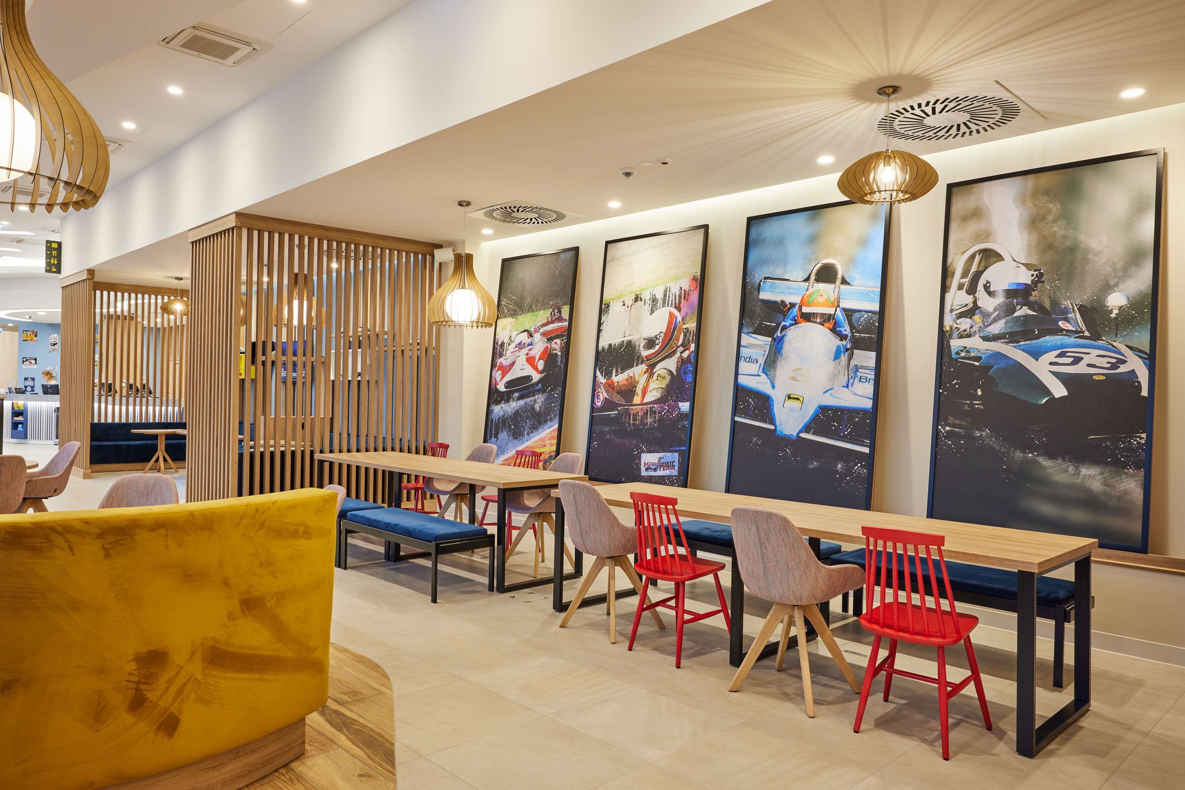 A modern dining area with wooden tables and chairs, large posters on the wall, and a yellow sofa.