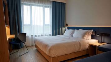 Una habitación de hotel moderna con una cama de madera, un escritorio, una silla y un ventanal con cortinas.