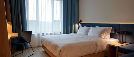 Una habitación de hotel moderna con una cama de madera, un escritorio, una silla y un ventanal con cortinas.