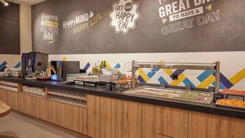 Una barra de desayuno con diversas opciones de alimentos, una máquina de café y decoración mural inspiradora.