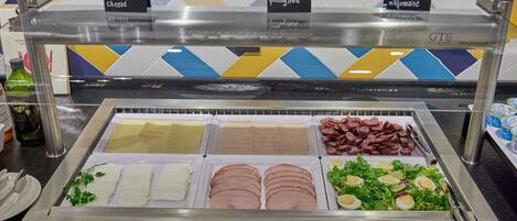 Un bufé con diversas opciones de comida, incluyendo queso, jamón y ensaladas.