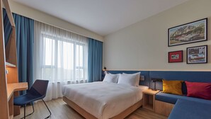 Una habitación de hotel con cama, escritorio, silla, sofá y ventana con cortinas.