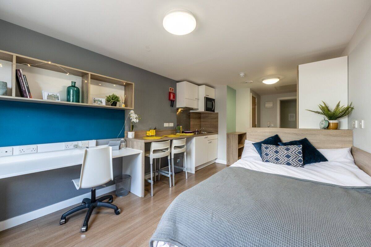 A modern bedroom with a large bed, a desk, and a kitchenette.