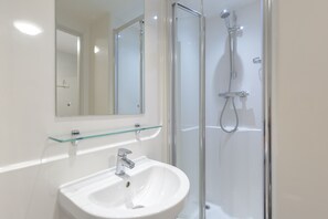 A bathroom with a glass shower enclosure, a white sink, and a glass shelf above the sink. - JOIVY Affordable Edinburgh - Adults only (Edinburgh)