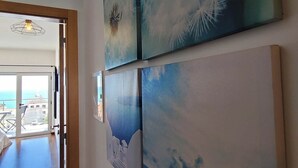 En hall med utsikt över havet genom en glasdörr, och konstverk på väggarna.