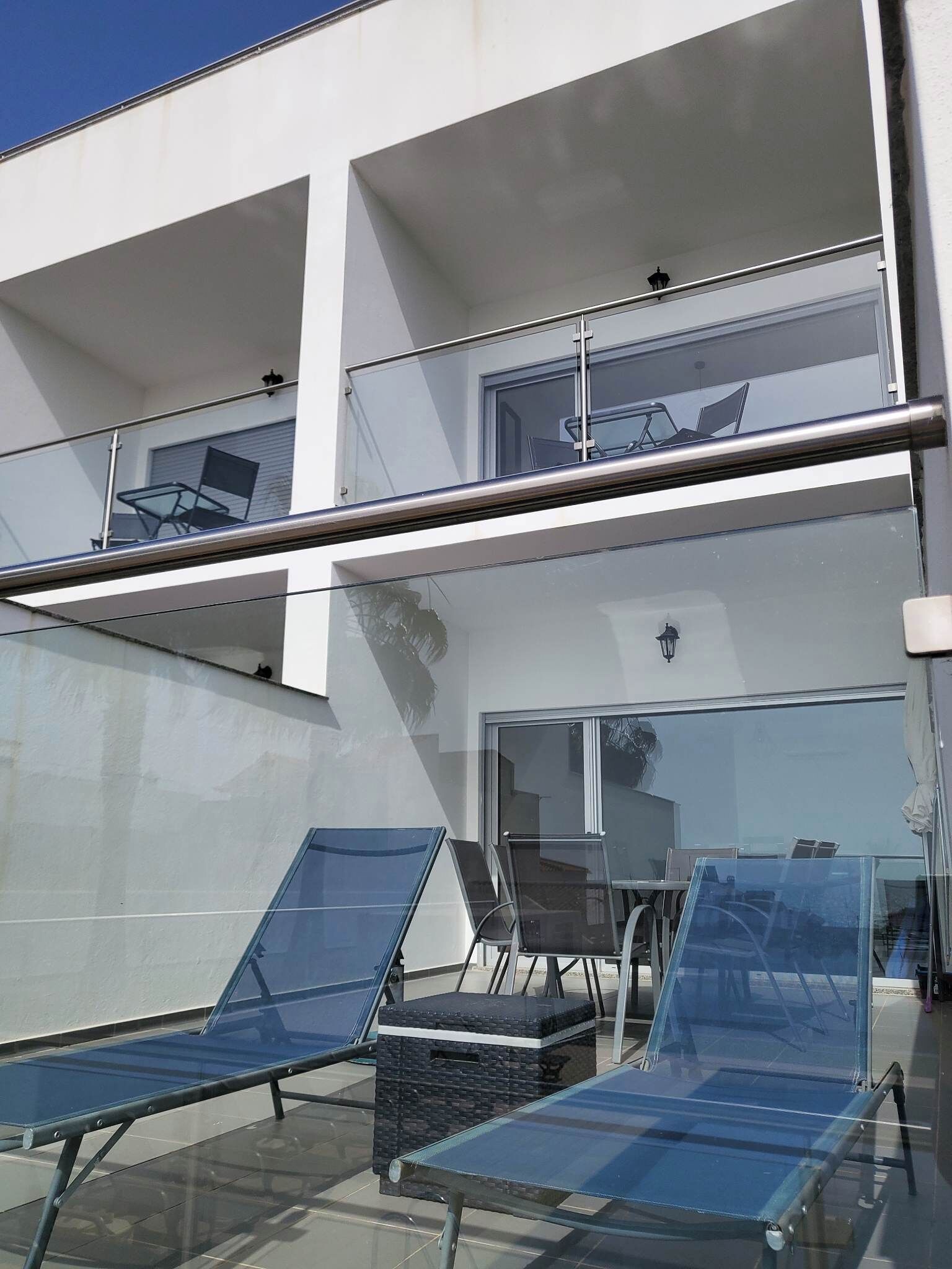 A modern two-story building with a glass balcony, outdoor seating area, and a clear view of the surrounding area.