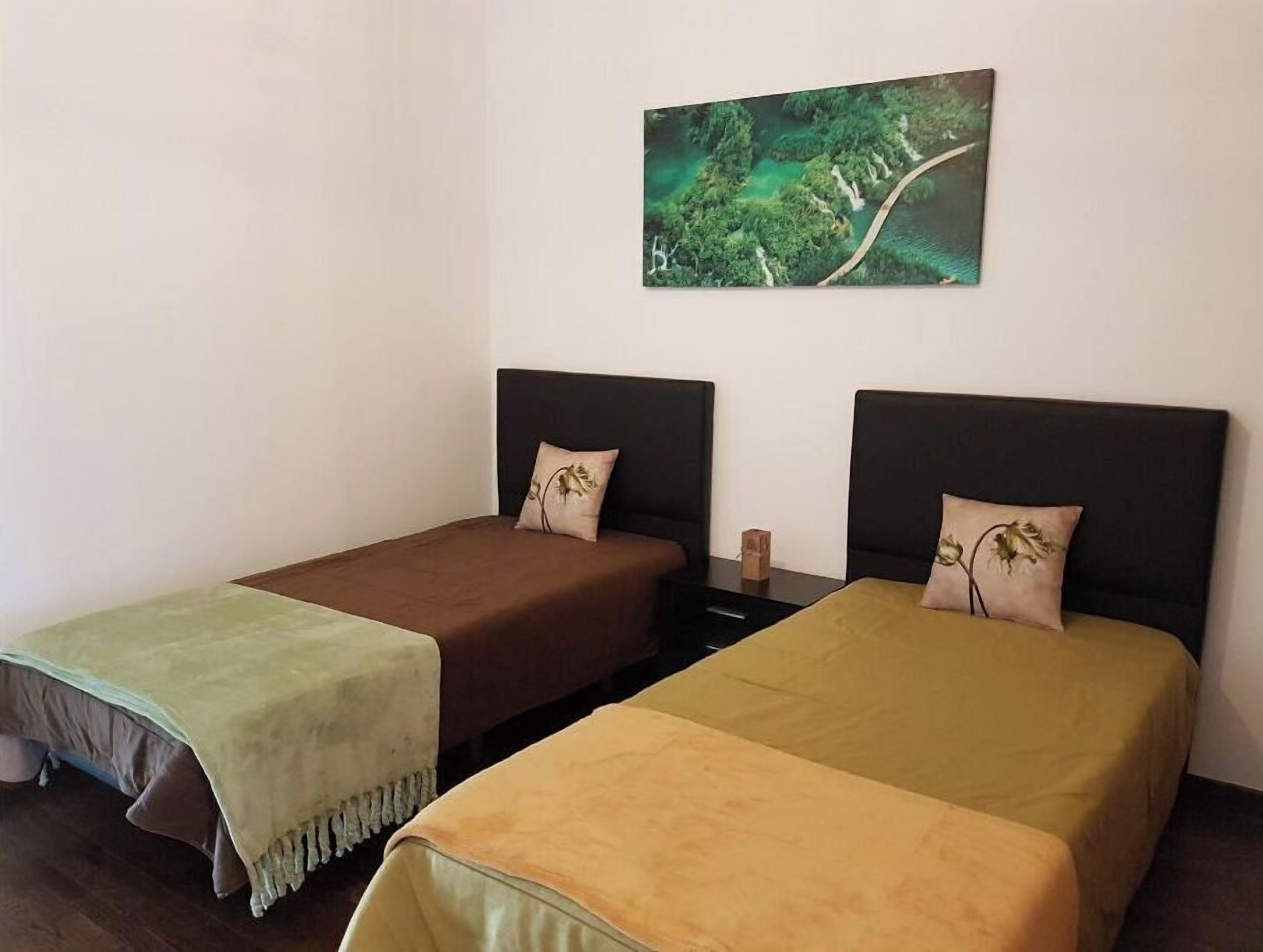 Twee enkele bedden met hoofdeinden, een kleine tafel en een boslandschap aan de muur.