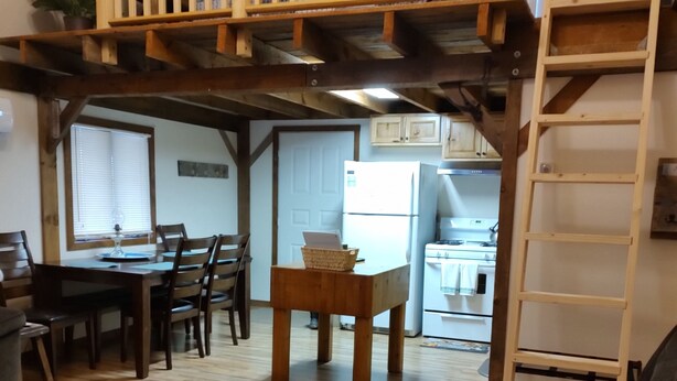 A cozy living room with a wooden floor, a dining area with a table and chairs, a kitchen in the background, and a staircase leading to an upper level. - Secluded Cabin Retreat – Peace, Privacy & Nature (Mansfield)
