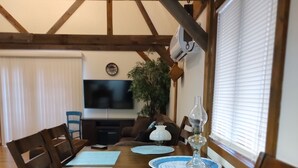 A dining area with a wooden table set for four, surrounded by chairs. A television is mounted on the wall in the background, and a plant is visible to the left. - Secluded Cabin Retreat – Peace, Privacy & Nature (Mansfield)