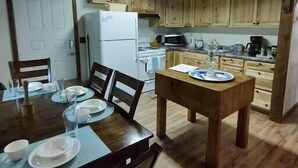 A rustic kitchen with wooden cabinets, a dining table set for four, and a refrigerator. - Secluded Cabin Retreat – Peace, Privacy & Nature (Mansfield)
