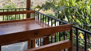 Un balcone in legno con tavolo e sedie, affaccia su un paesaggio montuoso con scarsa vegetazione.