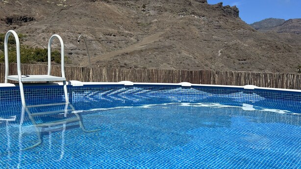 Una piscina con acqua cristallina e blu, circondata da una recinzione in legno, con montagne sullo sfondo.