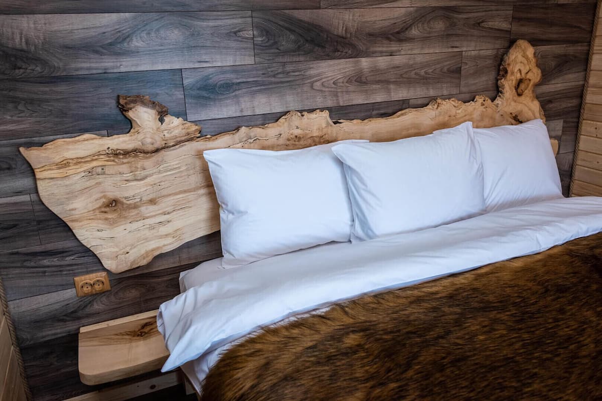 A bed with white bedding, a wooden headboard, and a large piece of wood art on the wall.