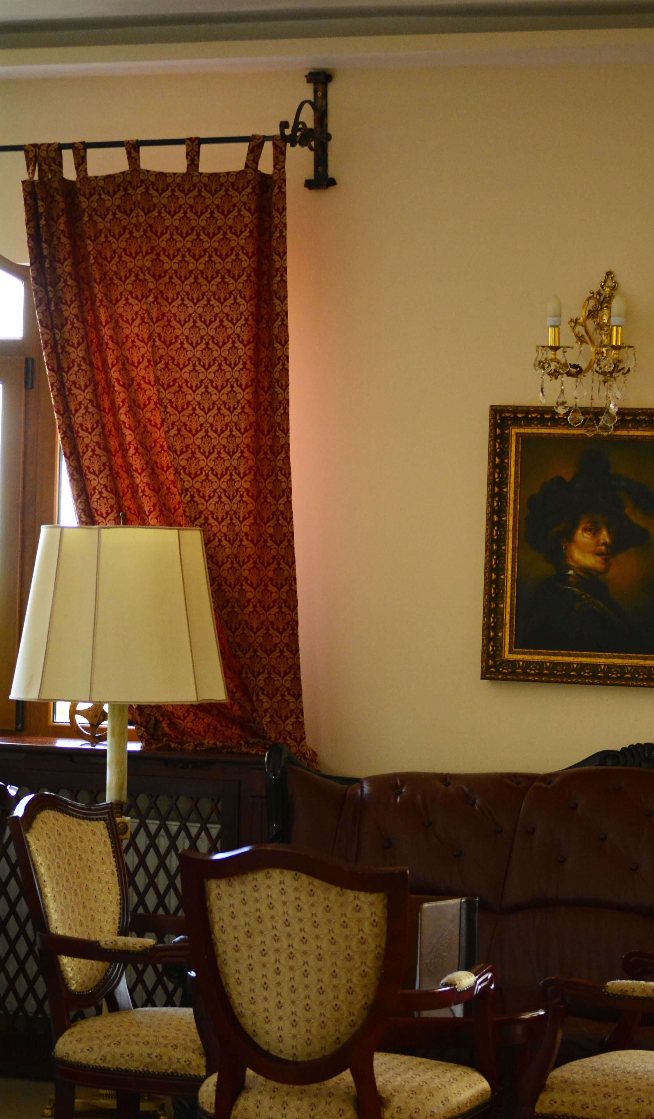 Une pièce avec des rideaux à motifs, un portrait encadré accroché au mur, une lampe et un canapé en bois agrémenté de coussins à motifs.