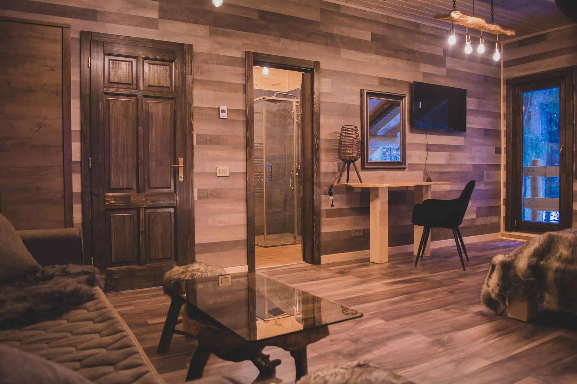 Ein gemütliches Wohnzimmer mit Holzboden, einem Glastisch, einer Couch und einem flauschigen Teppich.