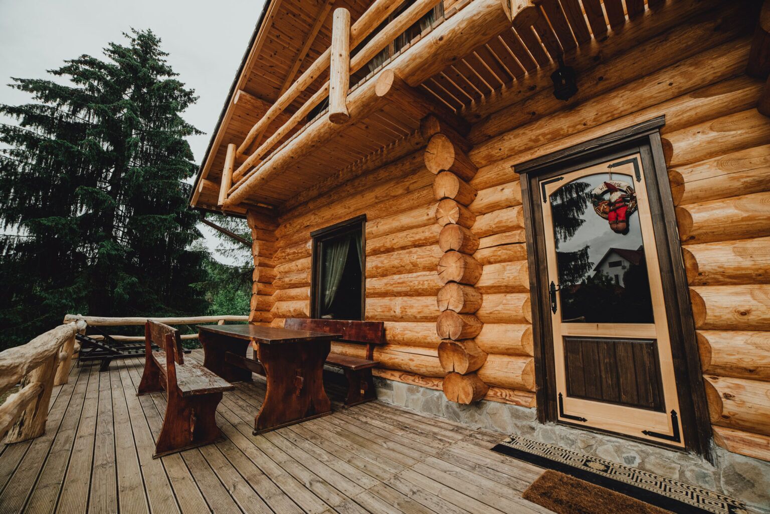 A log cabin with a deck, wooden benches, and a door with a picture.