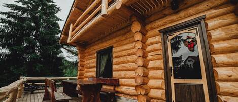 A log cabin with a deck, wooden benches, and a door with a picture.