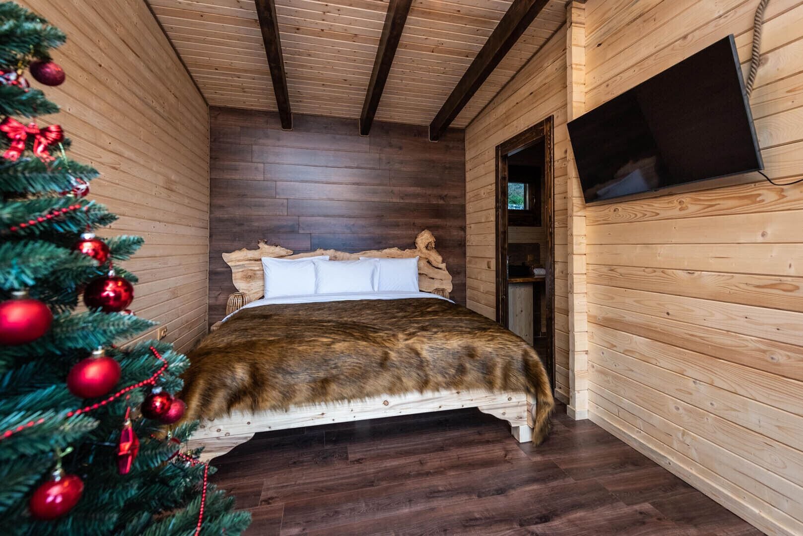 A wooden cabin room with a bed, a Christmas tree, and a television.