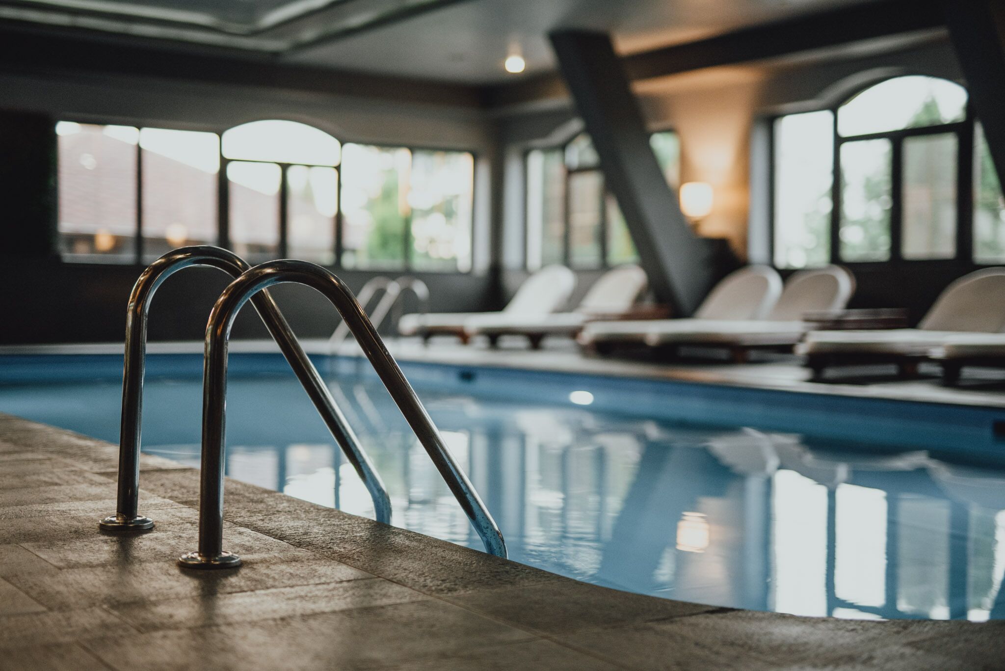 A swimming pool with metal railings, lounge chairs, and large windows allowing natural light.