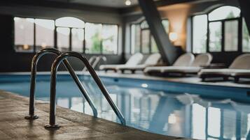 A swimming pool with metal railings, lounge chairs, and large windows allowing natural light.