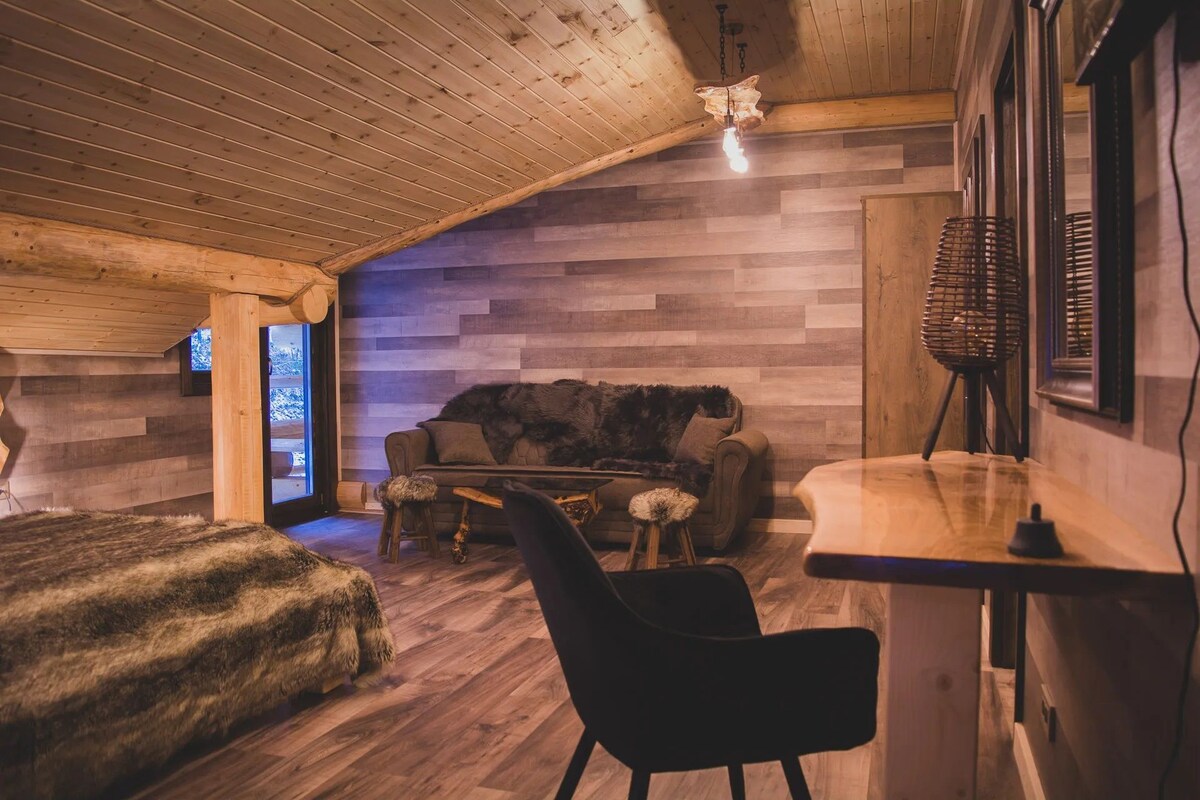 Un intérieur chaleureux avec un plafond en bois, un canapé recouvert de fourrure, une table basse en bois et un fauteuil noir.
