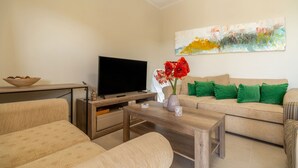 A living room with a sofa, a coffee table, a TV, and a painting on the wall. - 2 Bed House - Sleeps 5 - Garden - Parking - Wifi (Apokoronas)