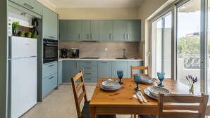 A modern kitchen with light blue cabinets, a wooden dining table, and a view of the outdoors through large windows. - 2 Bed House - Sleeps 5 - Garden - Parking - Wifi (Apokoronas)