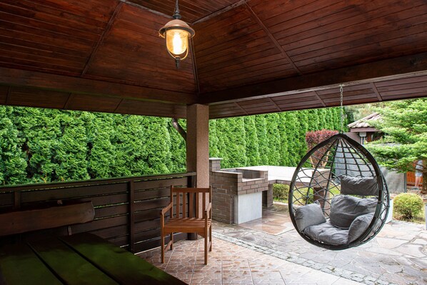A wooden deck with a hanging chair, a bench, and a stone-tiled patio.
