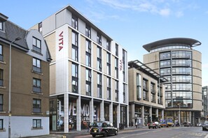 Un edificio moderno con un llamativo letrero 'VITA', que presenta una combinación de fachadas de ladrillo y vidrio, y una sección curva de vidrio a la derecha.