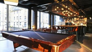A pool table in a modern bar area with large windows, a bar counter, and seating. - JOIVY at VITA Fountainbridge - Adults only (Edinburgh)