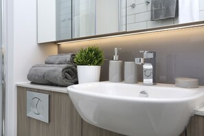 Un baño moderno con un lavamanos blanco, una planta en maceta, una toalla y un dispensador de papel higiénico.