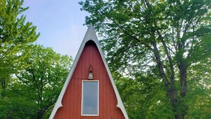 A red A-frame cabin with a balcony, surrounded by greenery. - The Gnome Home Cottage located near white mountain NH (Campton)