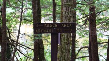 A directional sign in a forested area with a path leading to the beach and Abenaki Trail.