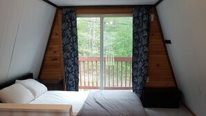A small, attic-style bedroom with a sloped ceiling, two beds, a wooden ladder, and a balcony with a wooden railing. - The Gnome Home Cottage located near white mountain NH (Campton)
