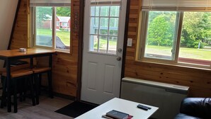 A cozy cabin with a loft bedroom, a dining area, and a living space with a leather couch and a small table. - The Gnome Home Cottage located near white mountain NH (Campton)