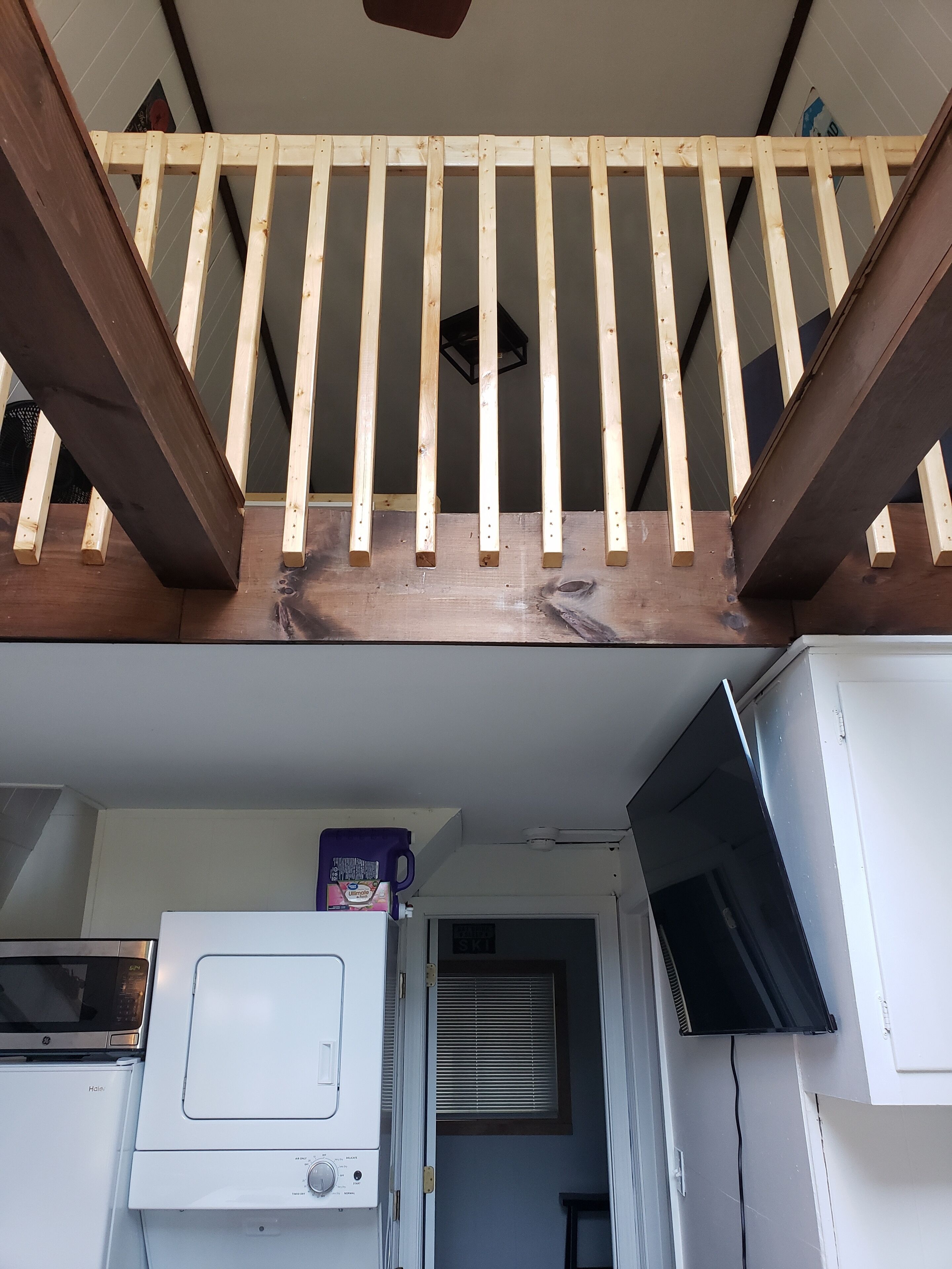 Un escalier en bois avec une rampe, un lave-linge blanc et un four à micro-ondes posés sur le sol.