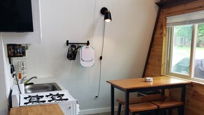 A compact kitchen with a gas stove, a sink, and a wooden table with stools. - The Gnome Home Cottage located near white mountain NH (Campton)